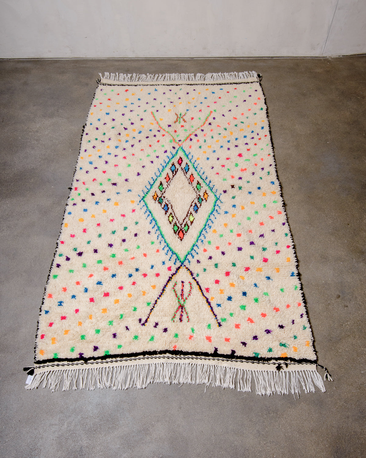 Berberlin Azilal rug made of cream sheep’s wool and colourful cotton laying on concrete floor.